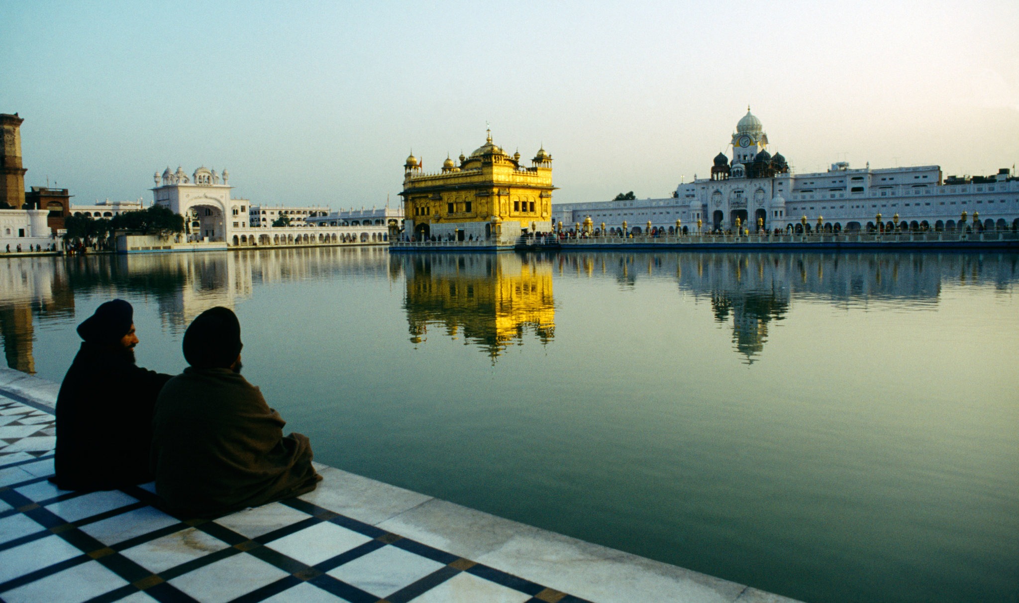 A landscape shot of Amritsar India Sri Harmandir Sahib (golden Temple) with two men sat in the foreground.