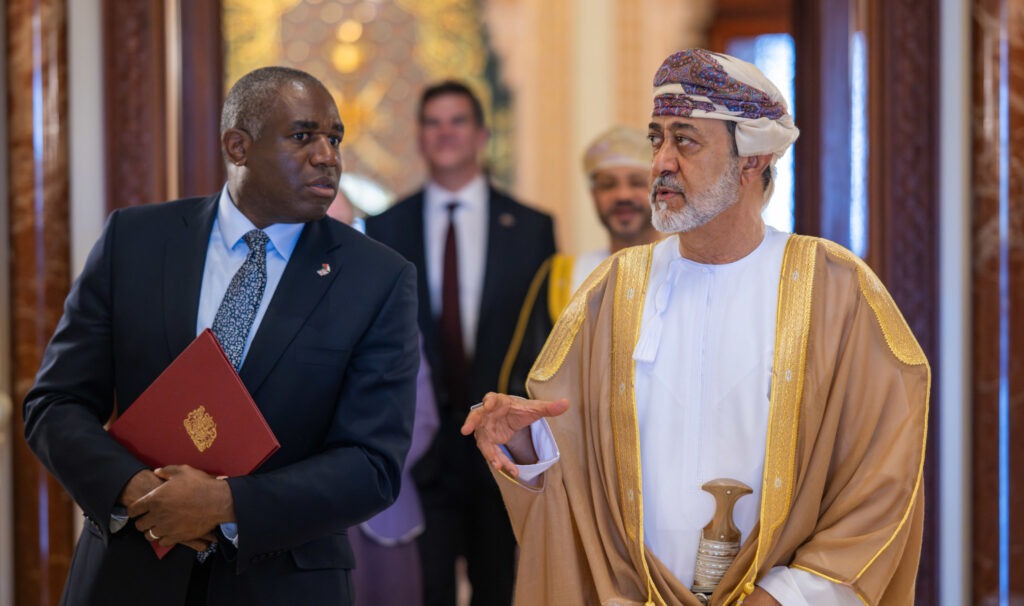 David Lammy holds a red folder as he walks towards the camera with the Sultan of Oman