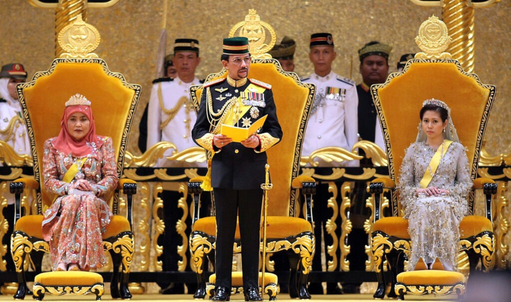2PBB2EE Brunei's Sultan Hassanal Bolkiah, center, speaks to the audience while Queen Saleha, left, and Queen Asrinaz Mazhar, right, look on at the throne hall of Istana Nurul Iman to mark his 61st birthday celebration in Bandar Seri Begawan , Saturday, July. 15, 2007. (AP Photo/Rudolf Portillo)