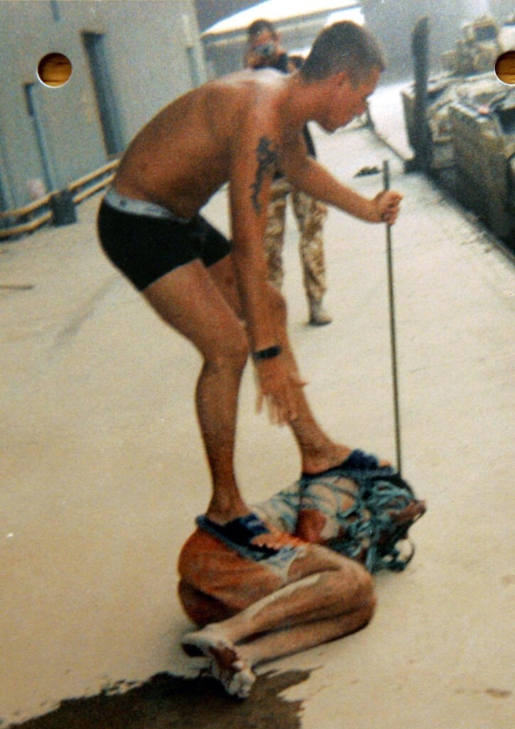 A British soldier stands on an Iraqi detainee at Camp Breadbasket in May 2003. (Photo: British court martial handout / Alamy)